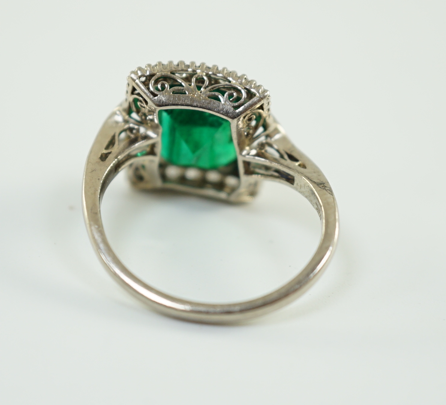 An Art Deco 18k white gold, emerald and diamond set square cluster dress ring, with shaped cut sapphire set shoulders, (a.f.)